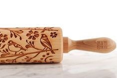 a wooden rolling pin decorated with birds and flowers on a marble countertop next to a white background