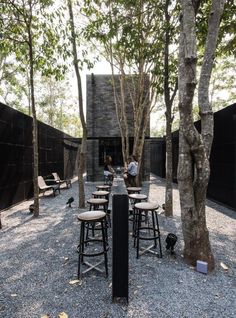 people are sitting at tables in the middle of a courtyard with black walls and trees