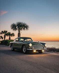 an old car is parked on the side of the road by the ocean at sunset