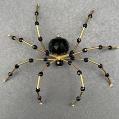 a black and gold spider made out of beads on a gray surface with the eyes closed