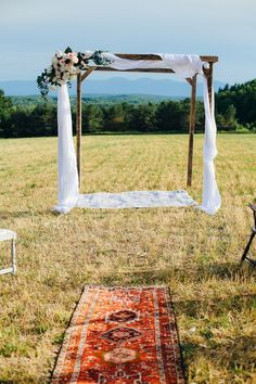 an outdoor wedding ceremony setup with white drapes and flowers on the altar, rug