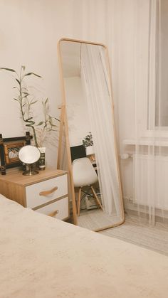 a mirror sitting on top of a wooden dresser next to a white bed in a bedroom