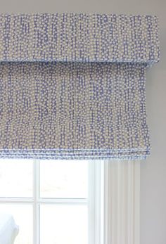 a blue and white patterned roman blind in front of a window