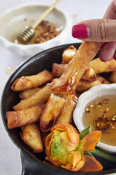 a person dipping sauce on some food in a bowl with other dishes around it and a flower