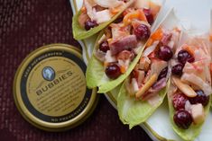 three lettuce wraps with fruit and meat on them next to a canister