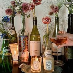 a table topped with lots of bottles and glasses filled with wine next to candles on top of a wooden table