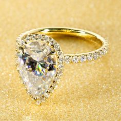 an engagement ring with a pear shaped diamond surrounded by small round brilliant diamonds on a golden background