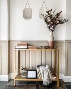 a wooden table topped with a vase filled with flowers next to a wall mounted mirror