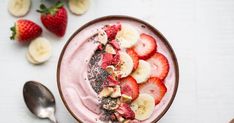 a bowl filled with fruit on top of a white table next to bananas and strawberries