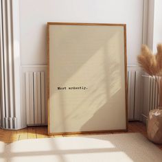 an empty frame sitting on the floor next to a vase with dry grass in it