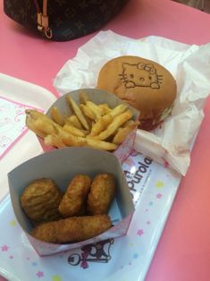 some food is sitting on a table next to a hello kitty cupcake and french fries