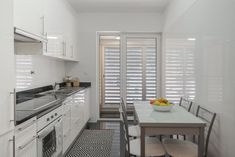 a kitchen with white walls and flooring has a dining table set for four in front of the window