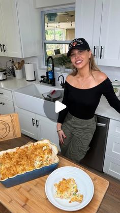 a woman standing in front of a casserole dish on a wooden cutting board