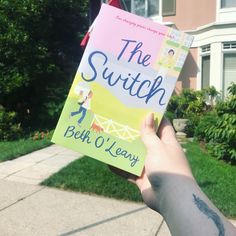 a person holding up a book in front of a house with the words the switch on it