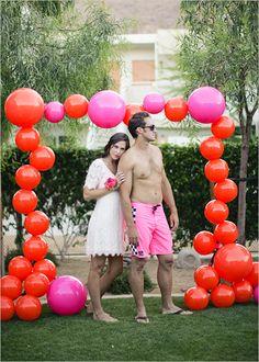 a man and woman standing in front of an arch made out of pink and red balloons