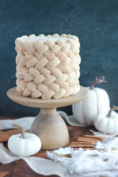 a white cake sitting on top of a wooden stand next to mini pumpkins and pretzels