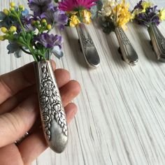 a person holding three spoons with flowers in them next to each other on a table