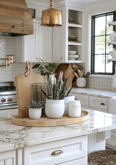 a kitchen with white cabinets and an island in front of the stove top is filled with potted plants