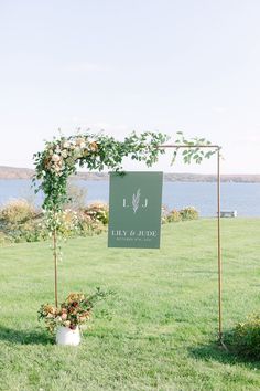 an outdoor ceremony setup with flowers and greenery on the grass, near a body of water