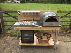 an outdoor pizza oven on wheels in front of a wooden fence with a basket next to it