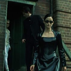 a woman in a black dress is walking down the street with two men behind her