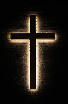 a lighted cross on a brick wall in the dark