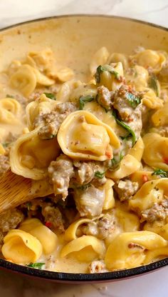 a skillet filled with pasta, meat and spinach on top of a table