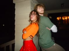 two people standing next to each other in front of a brick wall at night time