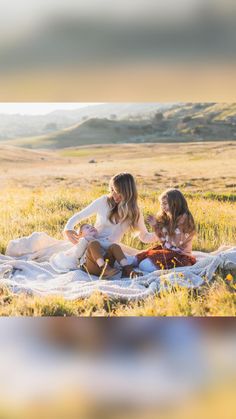 two women sitting on a blanket in the middle of a field