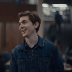 a young man smiling and wearing a denim jacket