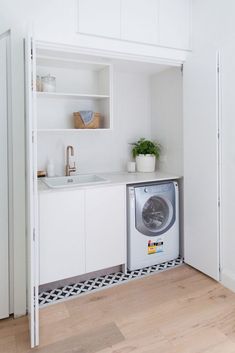 a washer and dryer are in the corner of this kitchen with white cabinets