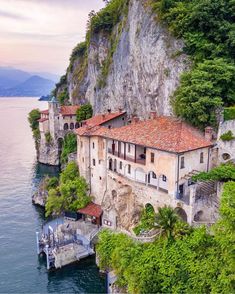 an old house on the edge of a cliff next to water with trees around it