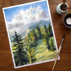 a watercolor painting of trees on a table next to a coffee cup and pen