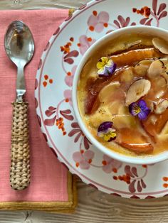 a bowl of soup with bananas and flowers on it next to a spoon, fork and napkin