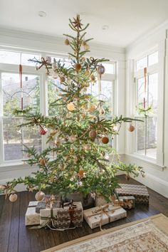 a christmas tree with presents under it in a living room next to a large window