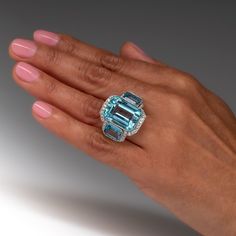 This stunning vintage cocktail ring is accented with one (1), bezel set, emerald cut natural aquamarine and flanked to each side by one (1), bezel set, emerald cut natural aquamarine. The gemstones are bordered with forty-six (46), bead set, old European cut diamonds. The shoulders of the ring are each accented with two (2), bead set, old European cut diamonds. The gemstones are bordered with milgrain edging. The ring measures 12.7mm at the top, rises 9.8mm above the finger, tapering to 2.0mm wi Luxury Emerald Cut Gemstone With 17 Jewels, Luxury Emerald Cut Ring With Gemstone Accents, Luxury Aquamarine Octagon Ring, Fine Jewelry Emerald Cut Topaz Ring Gia Certified, Elegant Emerald Cut Topaz Ring With 17 Jewels, Elegant Emerald Cut Topaz Ring, Luxury Octagon Aquamarine Ring, Gia Certified Emerald Cut Topaz Ring, Luxury Aquamarine Emerald Cut Rings