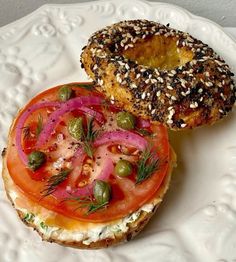 a bagel sandwich with tomatoes, onions and sprouts on it sitting on a white plate