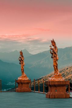 two statues on top of a building with mountains in the background