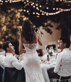 a woman in a wedding dress standing next to a man at a table with other people