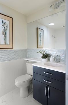 a white toilet sitting next to a bathroom sink under a framed painting on the wall