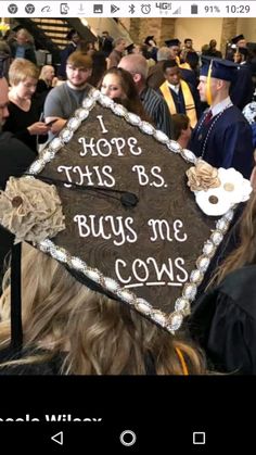 a graduation cap that says hope this bs buys me cows on it and people in the background