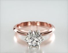 a rose gold engagement ring with a round cut diamond in the center, on a white background