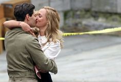 a man and woman kissing in front of a yellow caution line on the street with their arms around each other