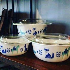 four glass casserole dishes sitting on top of a wooden table with blue and green designs