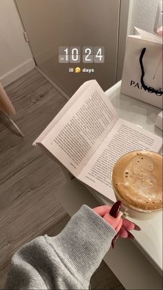 a person is reading a book and holding a cup of coffee