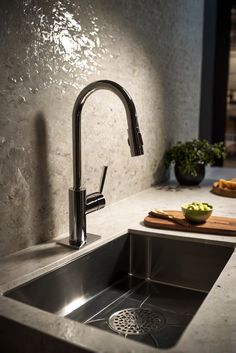 a kitchen sink with a cutting board on the counter and some fruit in the bowl