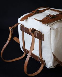 a white canvas bag with brown leather straps on a black background, showing the bottom part of the bag