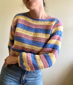 a woman wearing a multicolored striped sweater and jeans with her hands on her hips