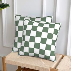 two green and white checkered pillows sitting on top of a wooden bench next to a potted plant