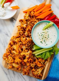 a wooden cutting board topped with carrots and celery next to a bowl of ranch dressing